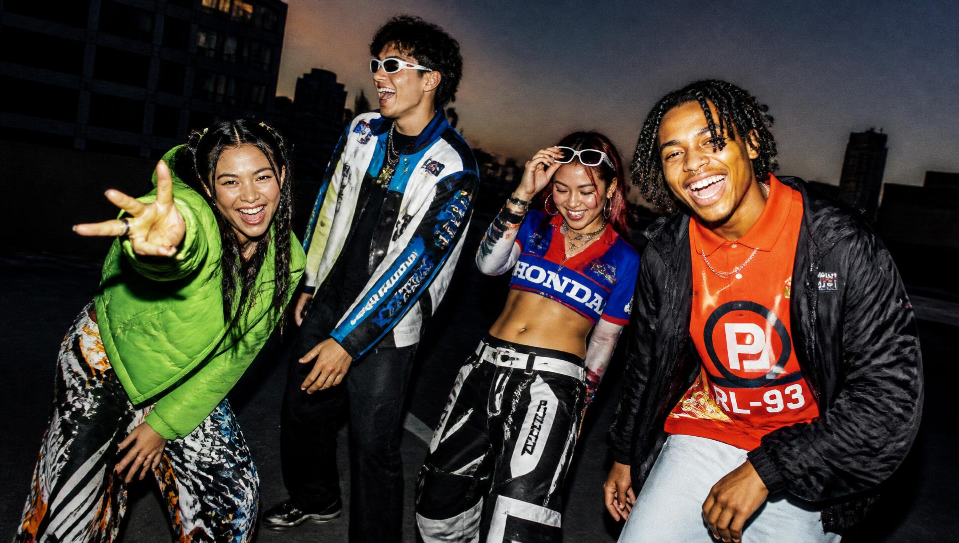 Four friends in bold streetwear posing on an urban rooftop at dusk